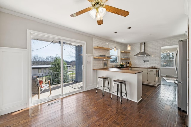 kitchen with visible vents, a peninsula, freestanding refrigerator, dark wood-style floors, and wall chimney exhaust hood