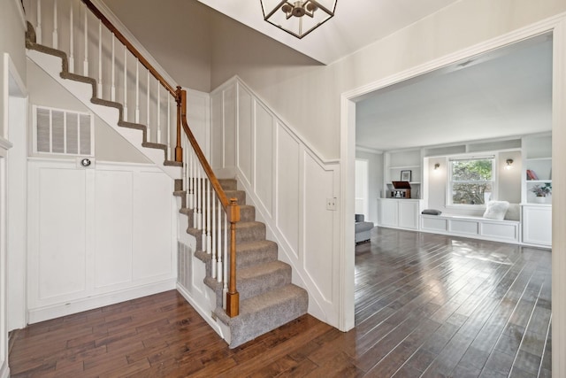 stairway featuring a decorative wall, built in shelves, visible vents, and wood finished floors