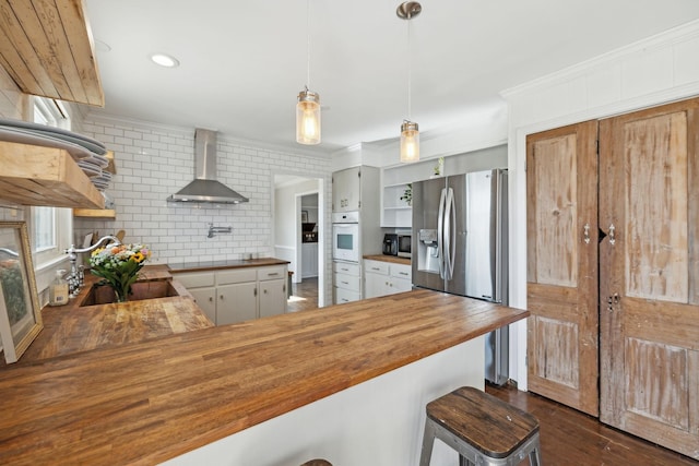 kitchen with ornamental molding, open shelves, appliances with stainless steel finishes, wall chimney range hood, and wooden counters