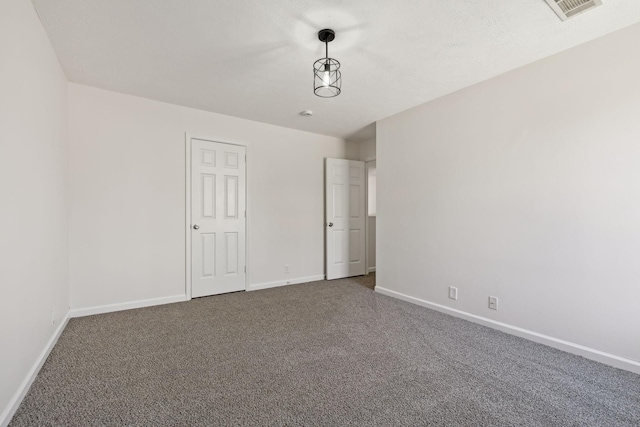 spare room featuring dark colored carpet, visible vents, and baseboards