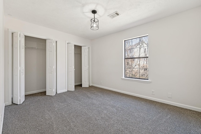 unfurnished bedroom featuring baseboards, carpet floors, visible vents, and multiple closets