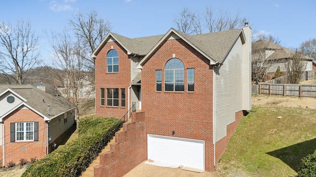 traditional-style home featuring brick siding, a chimney, fence, a garage, and driveway