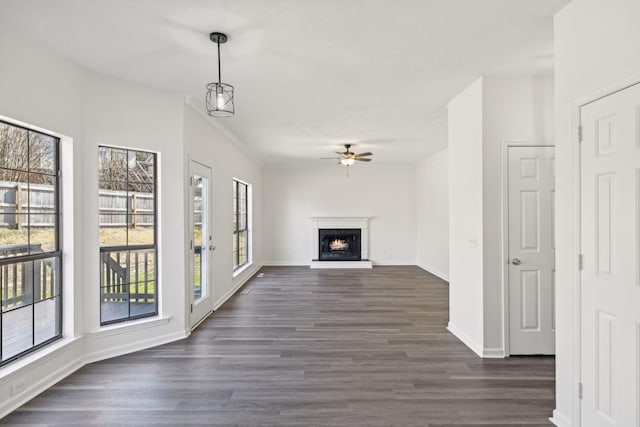 unfurnished living room with ceiling fan, baseboards, a lit fireplace, dark wood finished floors, and crown molding