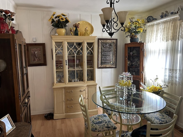 dining space with light wood-style flooring, ornamental molding, a decorative wall, and a notable chandelier