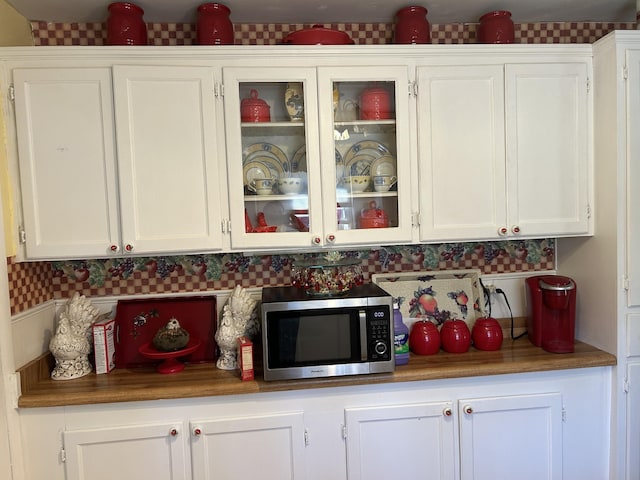 kitchen with stainless steel microwave, glass insert cabinets, and white cabinetry