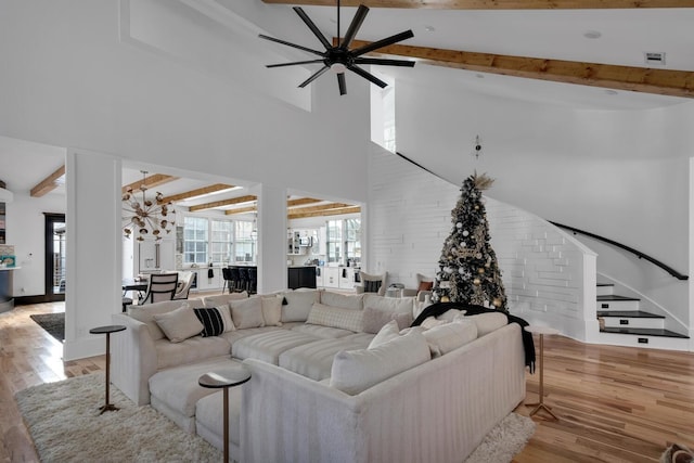 living area featuring light wood-type flooring, beamed ceiling, and ceiling fan with notable chandelier