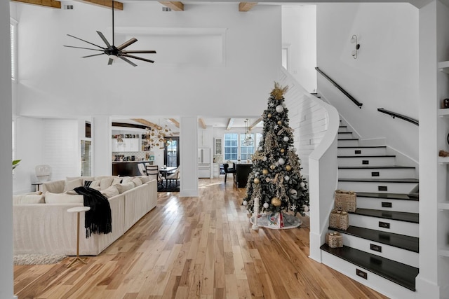 living area featuring a ceiling fan, a towering ceiling, light wood-style floors, stairway, and beamed ceiling