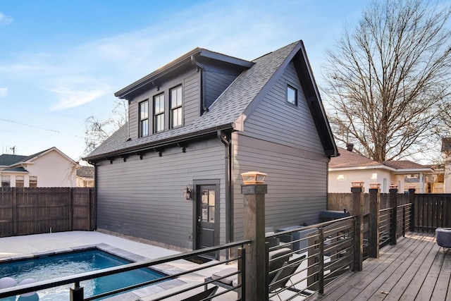 rear view of house featuring a shingled roof, fence, a deck, and a fenced in pool