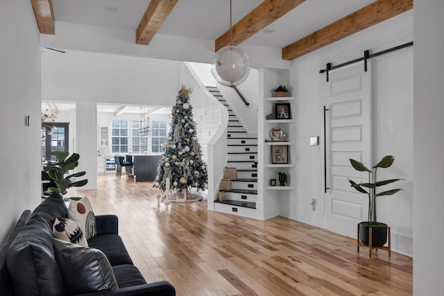 living area featuring a barn door, a chandelier, beamed ceiling, hardwood / wood-style floors, and stairs