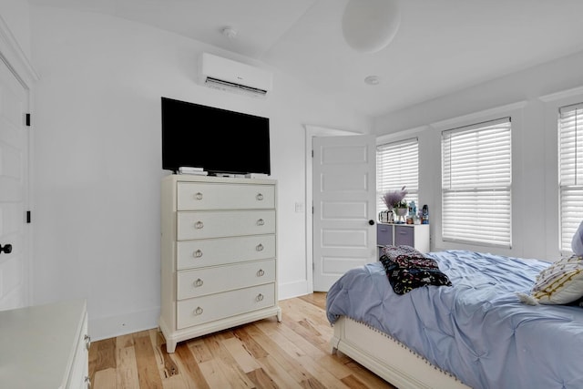 bedroom with light wood-style flooring, baseboards, and a wall mounted AC