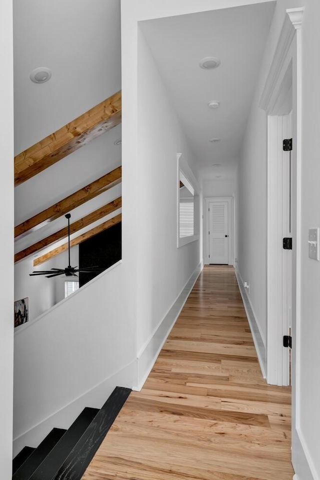 hall with light wood-style flooring, baseboards, and beamed ceiling