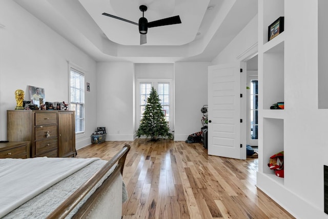 bedroom featuring a ceiling fan, a raised ceiling, light wood-style flooring, and baseboards