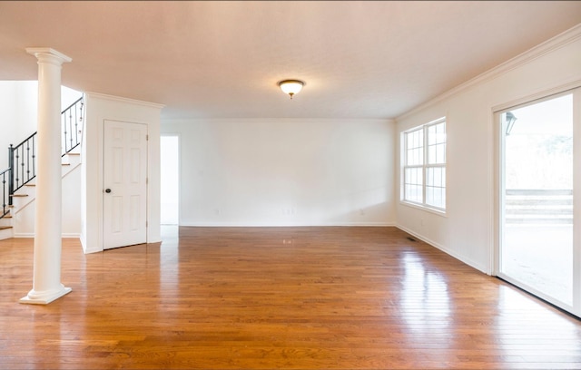 spare room with decorative columns, stairway, light wood-style flooring, ornamental molding, and baseboards