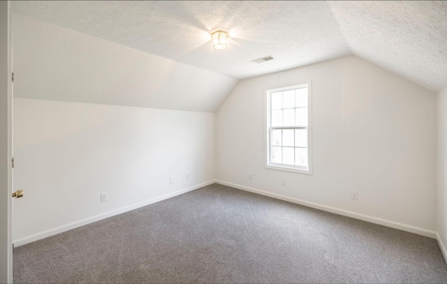 additional living space featuring a textured ceiling, carpet floors, visible vents, and baseboards