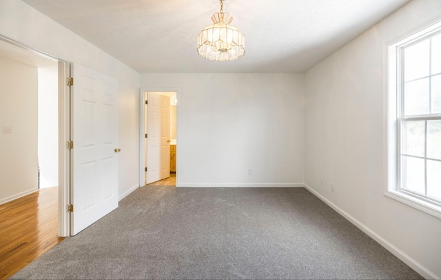 carpeted empty room with a chandelier and baseboards