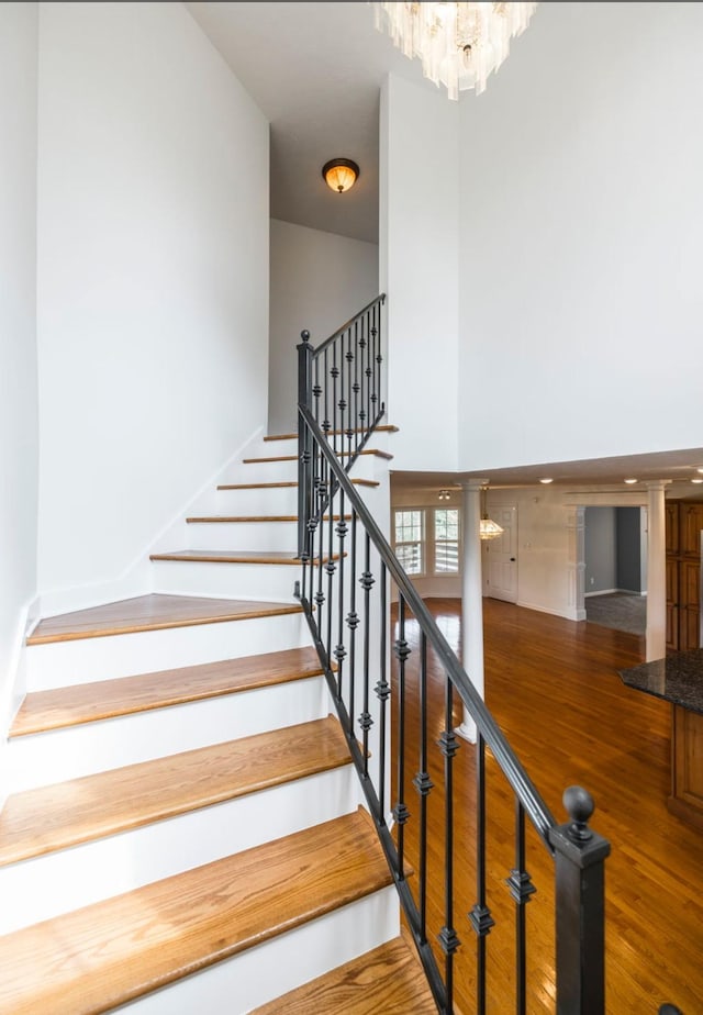 stairs with a chandelier, wood finished floors, and a towering ceiling