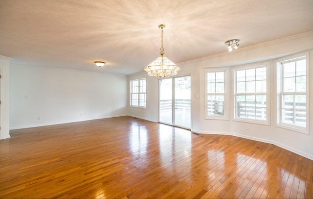 empty room featuring baseboards, crown molding, a chandelier, and hardwood / wood-style floors