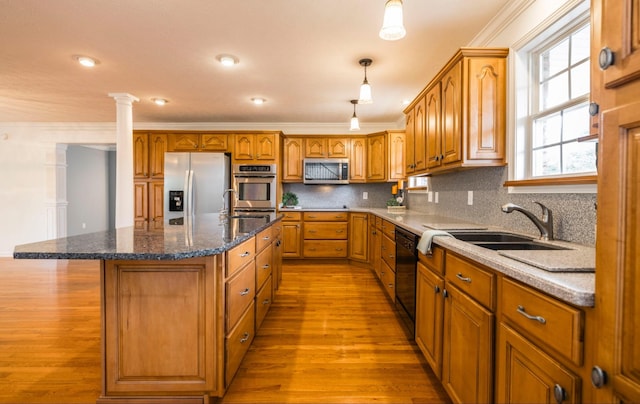 kitchen featuring brown cabinets, decorative columns, stainless steel appliances, tasteful backsplash, and a kitchen island with sink