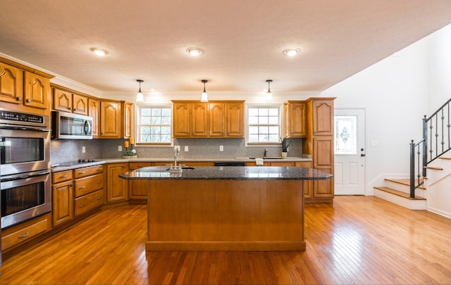 kitchen featuring appliances with stainless steel finishes, brown cabinetry, an island with sink, and tasteful backsplash