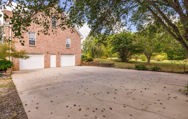 view of side of property featuring concrete driveway, brick siding, and an attached garage