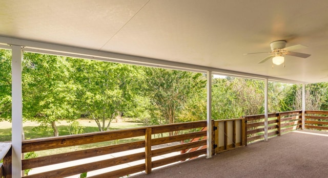 unfurnished sunroom with a ceiling fan and a view of trees