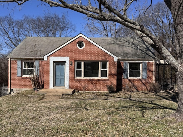 view of front of house featuring a front yard, brick siding, and roof with shingles