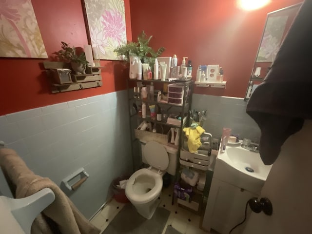 half bath with a wainscoted wall, tile walls, toilet, and vanity