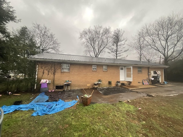 rear view of house with entry steps, metal roof, brick siding, and a patio