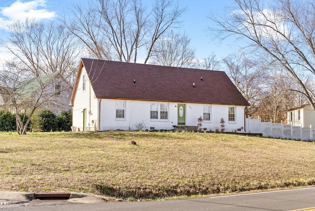 new england style home with a front lawn, a shingled roof, fence, and brick siding