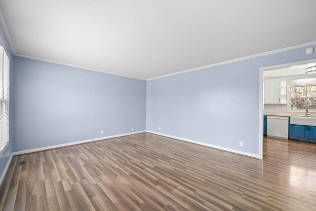 spare room with a sink, ornamental molding, wood finished floors, and baseboards