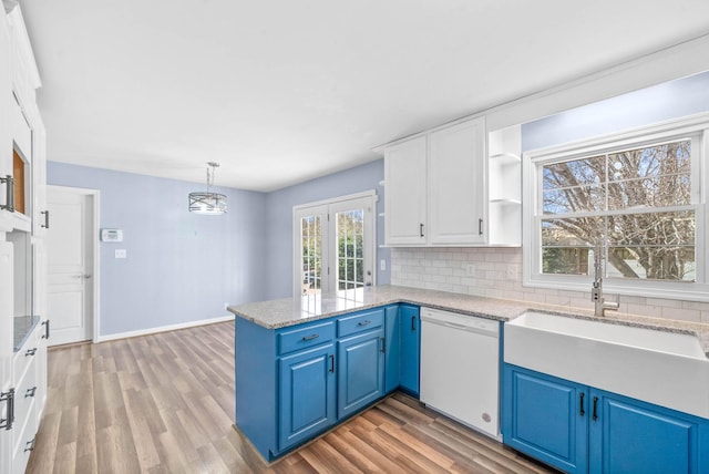 kitchen with a peninsula, a sink, white cabinets, decorative backsplash, and dishwasher