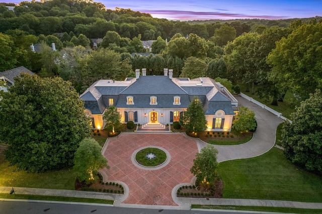 view of front of house featuring driveway, a forest view, a chimney, roof with shingles, and a front yard