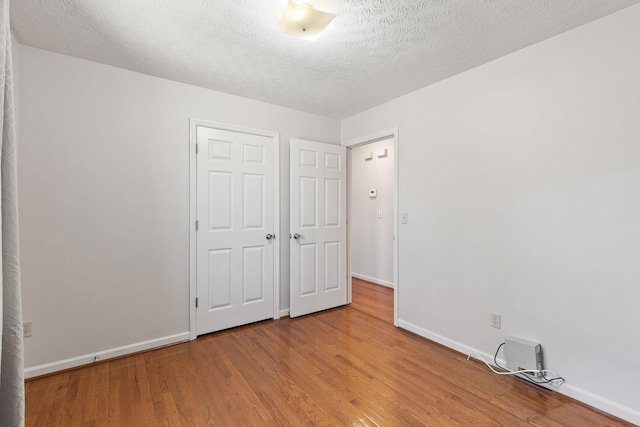 unfurnished bedroom featuring a textured ceiling, baseboards, and wood finished floors