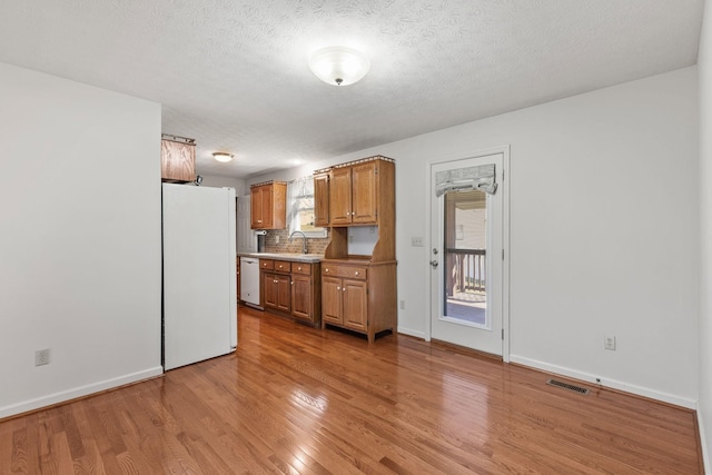 kitchen featuring white appliances, tasteful backsplash, light wood finished floors, visible vents, and brown cabinets