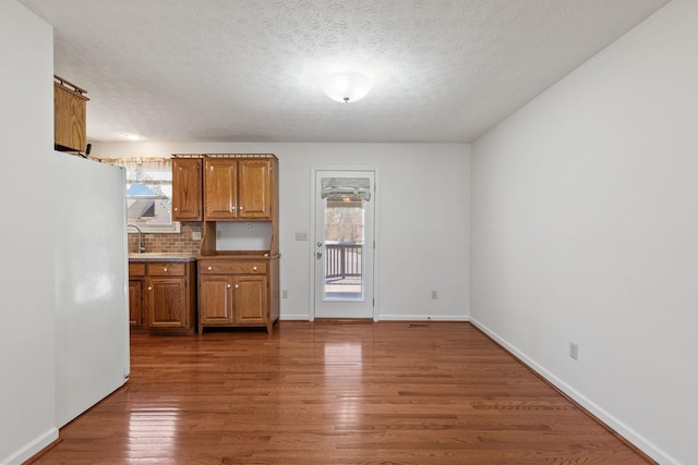 kitchen featuring a textured ceiling, wood finished floors, baseboards, tasteful backsplash, and brown cabinetry