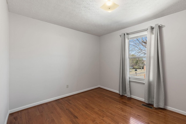 empty room with visible vents, a textured ceiling, baseboards, and wood finished floors