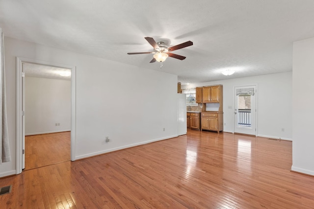 unfurnished living room with ceiling fan, a textured ceiling, visible vents, baseboards, and light wood-type flooring