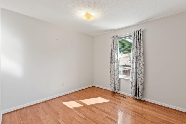 unfurnished room with visible vents, a textured ceiling, baseboards, and wood finished floors