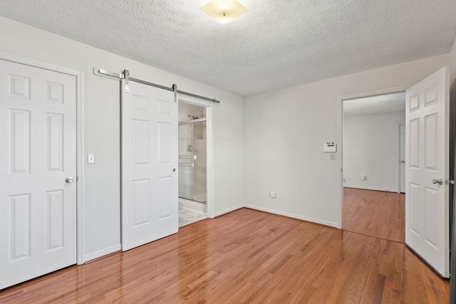 unfurnished bedroom with light wood-type flooring, a barn door, baseboards, and a textured ceiling