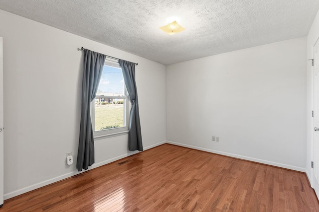 unfurnished room with a textured ceiling, baseboards, and wood finished floors