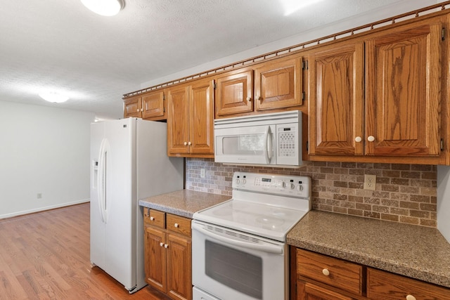 kitchen featuring decorative backsplash, brown cabinetry, a textured ceiling, light wood-type flooring, and white appliances