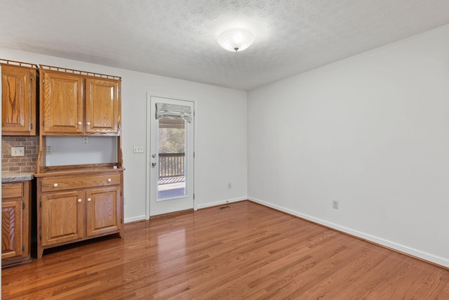 unfurnished dining area with baseboards, a textured ceiling, and light wood-style floors