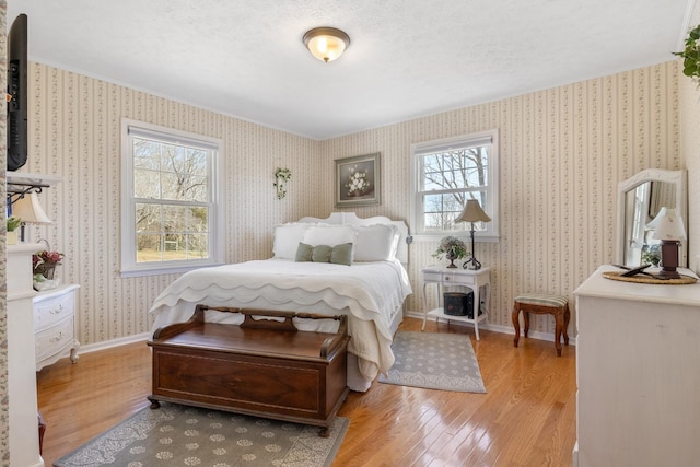 bedroom featuring baseboards, light wood-style floors, a textured ceiling, and wallpapered walls