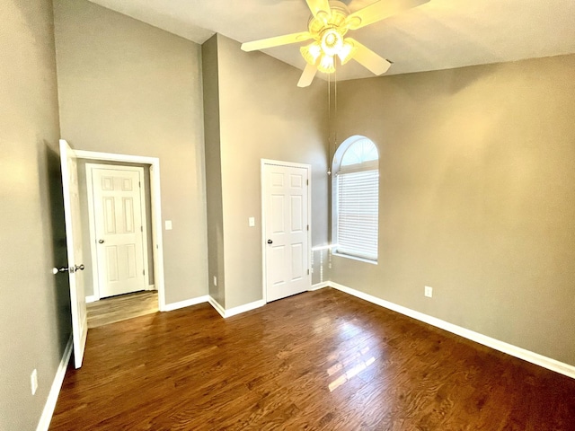 unfurnished room with ceiling fan, high vaulted ceiling, dark wood-type flooring, and baseboards