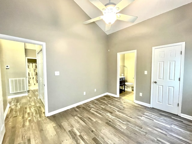 unfurnished bedroom with ensuite bathroom, high vaulted ceiling, wood finished floors, visible vents, and baseboards