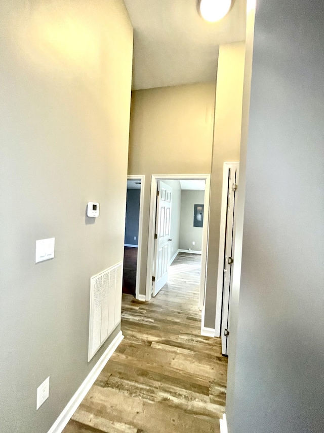 hallway featuring baseboards, a high ceiling, visible vents, and wood finished floors