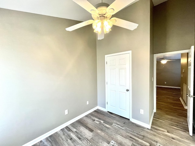 unfurnished bedroom featuring a ceiling fan, a towering ceiling, baseboards, and wood finished floors