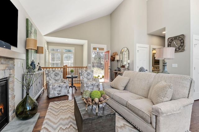 living area with high vaulted ceiling, a stone fireplace, and dark wood-type flooring