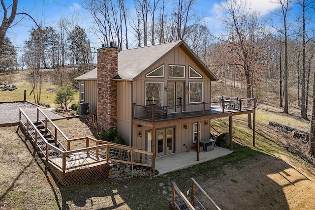 back of house with a patio area, a deck, board and batten siding, and roof with shingles