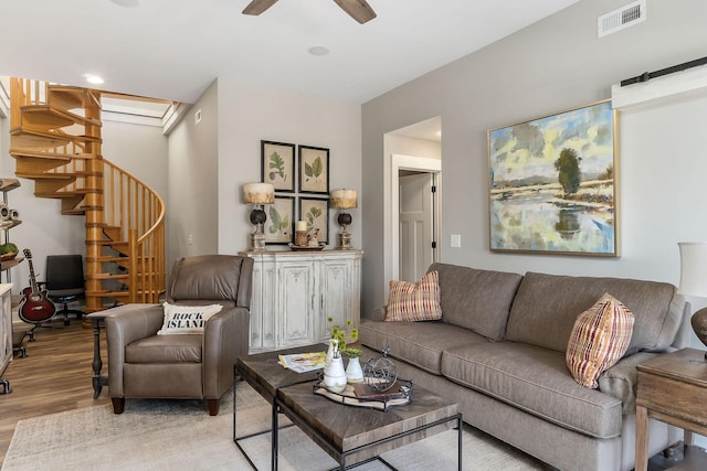 living room featuring light wood finished floors, stairway, visible vents, and a ceiling fan